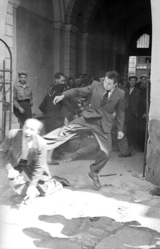 Un uomo prende a calci un ebreo in mezzo alla strada durante un pogrom