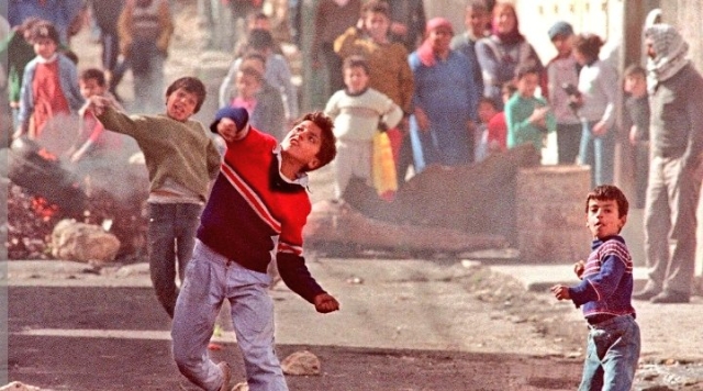 Un ragazzo palestinese lancia una pietra in mezzo alla strada durante la prima Intifada